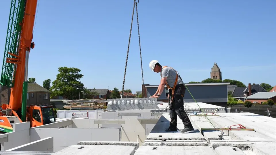 Hijskeurmeesters 11 Monteur met valbeveiliging begeleidt een betonelement aan de kraan op de bouwplaats